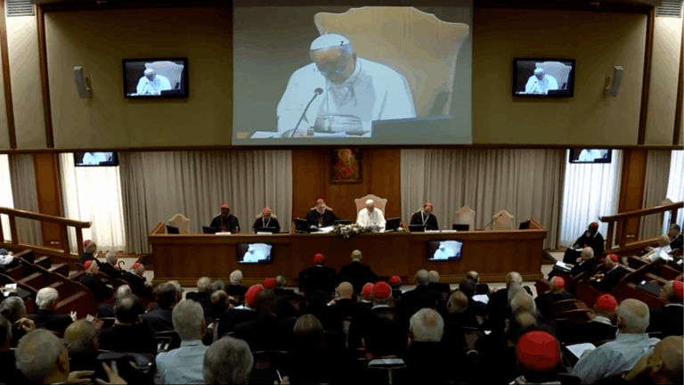 Papa Leão XIV na sessão de encerramento do Consistório extraordinário no Vaticano, sentado à mesa principal diante dos cardeais reunidos na Sala do Sínodo. Ao fundo, um telão exibe a imagem do Pontífice durante seu discurso.