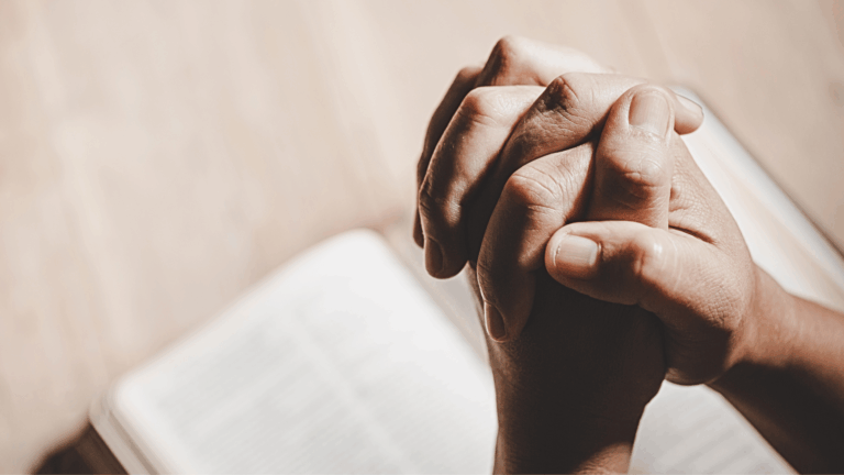 Mãos entrelaçadas em oração sobre uma Bíblia aberta, simbolizando um momento de fé, meditação e leitura da Palavra de Deus.