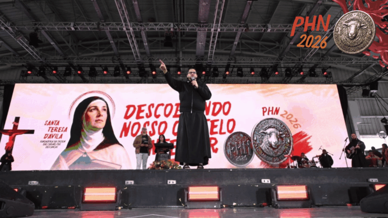 Padre Ailton prega no palco principal do PHN 2026 diante de milhares de participantes, com painel ao fundo destacando Santa Teresa d