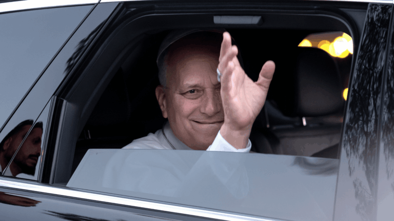 O Papa Leão XIV acena de dentro de um carro preto, com a janela abaixada.