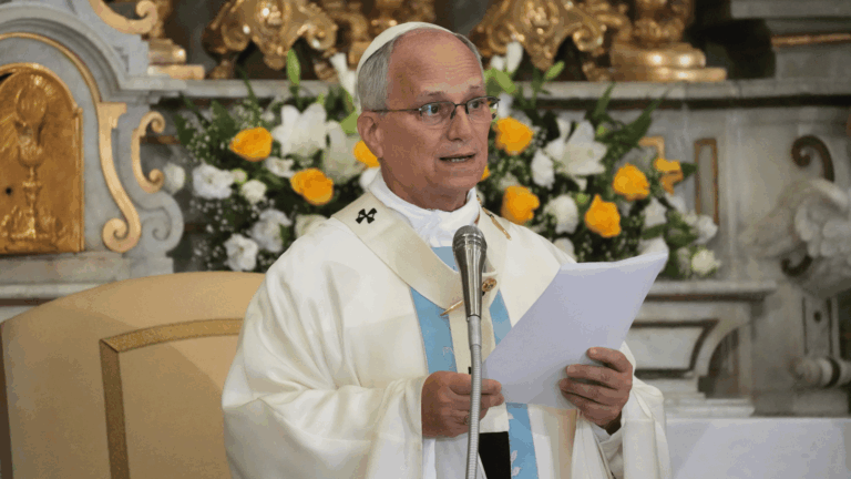 A imagem ilustra o Papa Leão XIV, paramentado com vestes litúrgicas brancas com detalhes azuis, durante a celebração de uma Missa.