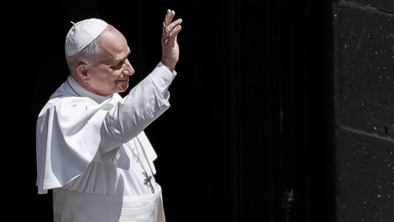 Papa Leão XIV acena aos fiéis enquanto deixa um edifício durante seu período de descanso em Castel Gandolfo, usando veste branca e solidéu.