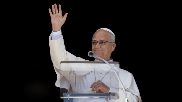 A imagem ilustra o Papa Leão XIV, com suas habituais vestes pontifícias, diante de um púlpito e um microfone. Ele tem o braço direito erguido, acenando.