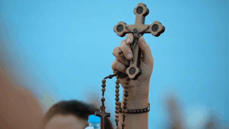 Fiel ergue um crucifixo de madeira com a imagem de Jesus Cristo e segura um terço durante momento de oração.