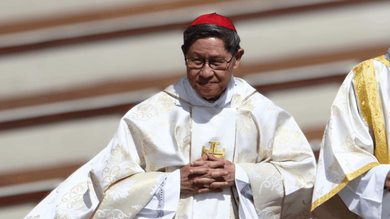 Cardeal Luis Antonio Tagle, com paramentos litúrgicos brancos e solidéu vermelho, mantém as mãos unidas durante celebração.
