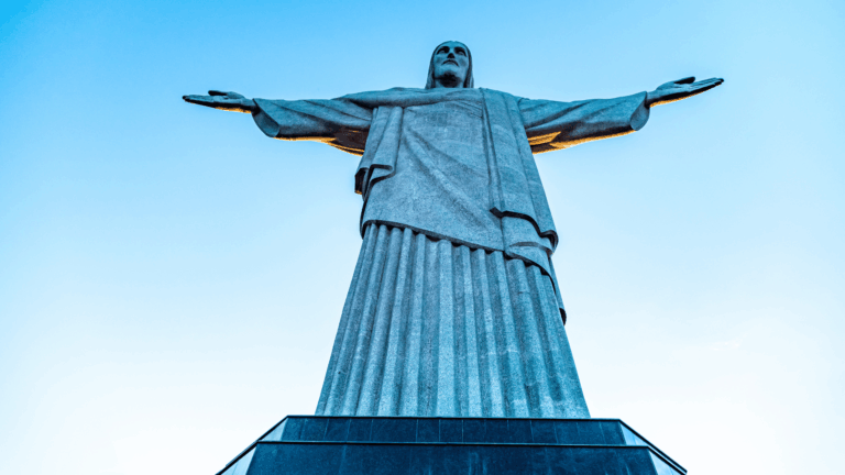 Monumento do Cristo Redentor, no Rio de Janeiro, visto de baixo, com os braços abertos diante do céu azul.